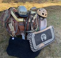 Western saddle with attached saddle bags, horse blankets, bridles, reins, two helmets, and horse pads displayed outdoors on saddle stand.