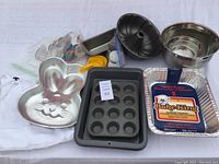 Overview photo showing various baking pans including bunny-shaped cake mold, muffin pan, bundt pan, mixing bowl, loaf pan, and disposable foil pans.