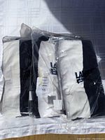 Three black and white folded and sealed Lands' End beach towels stacked on white surface.