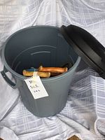Rubbermaid gray garbage can with black lid and wooden handled saws inside
