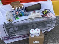 Photo showing layout of items including ironing board, fatigue mat, hand sanitizer bottles, cleaning wipes case, and other cleaning tools on fabric surface.