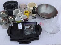 Full overview of lot showing Sunbeam griddle, stainless steel mixing bowls, stainless steel canisters, ceramic mugs, glass bowl, other glassware and accessories.