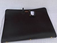 Black textured large portfolio's full front view with closure strap visible