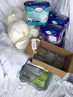 Photo shows multiple packages of TENA men's guards and overnight underwear protection items, including a cardboard box with grey clothing items and white plastic packages.
