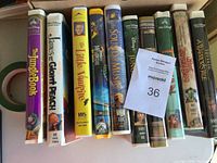 Photo of 10 VHS tapes arranged upright in a box with visible titles and covers.