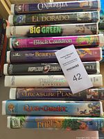 Stacked VHS movies showing movie titles and spine artwork for Cinderella, El Dorado, Big Green, The Black Cauldron, Beauty and the Beast, Inspector Gadget, The Princess Diaries, Treasure Planet, Quest for Camelot, One Hundred and One Dalmatians II.