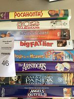 Top down view of stacked VHS tapes showing the spines with titles like Pocahontas, 101 Dalmatians, The Miracle Maker, Big Fat Liar, Dogs Go to Heaven 2, The Aristocats, Amazing Panda Adventure, Angels in the Outfield.