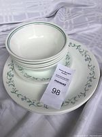 Stack of 4 bowls on top of 2 dinner plates showing Ivy with Hearts pattern with green trim and small blue and green hearts on a white background.
