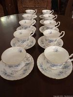 Ten sets of Royal Albert Blue Blossom china tea cups and saucers arranged on a wood table