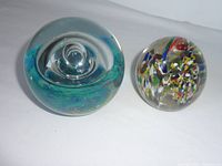 Top view of two glass paperweights, one blue/green with internal swirl and bubbles, one clear with colorful inclusions.