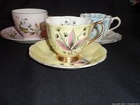 Three different vintage porcelain cups and saucers displayed showing floral designs and gold trim details.