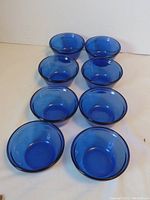 Top angled view showing the 8 cobalt blue Anchor Hocking bowls grouped closely together on a white background.