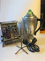 Photo showing the coffee percolator with green glass knob and black handle, toaster with metal ornate sides and toast rack in front.