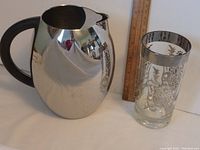 Full side view of stainless steel pitcher and etched glass with a ruler for scale