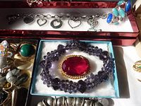 Silver-tone charm bracelet with heart charms, multi-stone ring, purple beaded necklace with red centerpiece, and assorted rings