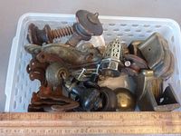 Plastic basket containing assorted wooden, brass, and ceramic furniture hardware pieces including drawer pulls and knobs.