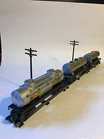Three silver Lionel tank cars arranged in line on track with two brown telephone poles for scale, showing the full set and details of cars.
