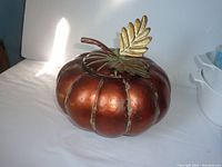 Top-front view of large copper-colored metal pumpkin with a removable lid featuring a gold leaf and stem detail.