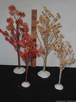 Two fall miniature trees including a 12-inch birch tree with yellow leaves and an 8-inch maple tree with red-orange leaves, standing on white bases with a ruler for scale.