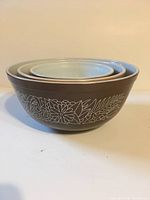 Side view of three nested Pyrex Woodland pattern mixing bowls, showing brown glass exterior with floral design.