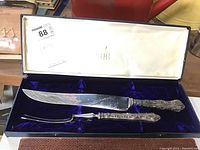 Birks carving set knife and fork displayed in blue velvet-lined box with ivory lid interior showing Birks' logo and price sticker.