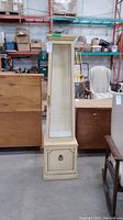 Front view of tall narrow curio cabinet with glass door and bottom storage compartment with brass handle.