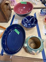 Four ceramic items displayed on a table including two Denby bowls, one Denby serving dish, and one decorative ceramic plant pot. Size stickers visible on two items.