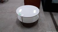 Round white glass coffee table with metal frame and wheels, showing top surface and lower shelf
