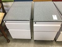 Two white mobile file cabinets side by side with gray upholstered tops shown from front