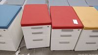 Photo showing multiple metal filing cabinets with cushioned tops in blue, red, and yellow colors, highlighting the red cushioned tops on two cabinets.