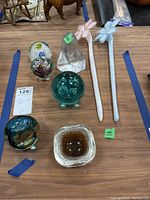 Full set of four glass paperweights, trinket dish, woman's head figure, and two Murano-style flowers arranged on table.