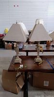 Pair of table lamps with carved bases and beige textured fabric shades on a table, showing overall condition and setup.