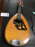 Front view of mandolin showing body, decorative leaf pickguard, and metal chin strap area.
