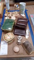 Photo showing multiple items on table including porcelain vase with floral design, wooden carved figurine, various pill and trinket boxes, small white ceramic sheep figurine, and coasters.