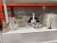 Wide view of the full lot showing the various glass and porcelain items including decanters, glasses, bowl, and packaging.