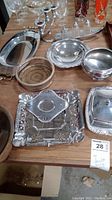 Several silver plate and stainless steel serving items including candle holder with wood base, trays, bowls, and butter dish.