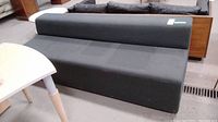 Front view of the dark grey upholstered sofa with rectangular backrest and wooden panel along the back.