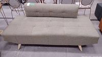 Full front view of the armless sofa showing tufted seat and backrest with wooden legs.