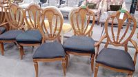 Row of four wooden dining chairs with black upholstered seats, showing two captain chairs with armrests at the ends and two side chairs in the middle.
