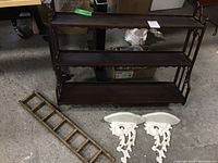 Three-level dark wood ladder-style shelf with scalloped edges and two white ornate wall floating shelves on the floor.