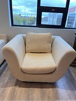 Front view of cream Fendi upholstered armchair with removable seat cushion and back pillow on wood floor under window