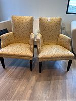 Pair of cushioned armchairs with patterned beige upholstery and wood legs on wooden floor.