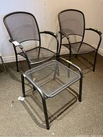 Two metal mesh exterior chairs and one small metal mesh table on carpeted floor.