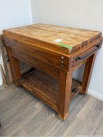 Front-left angle of the wood butcher block style kitchen table showing thickness and metal handle on side.