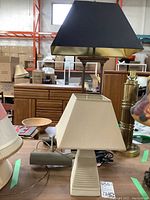 Three lamps on table: ceramic base with cream shade and two metal base lamps, one with black/gold trapezoid shade