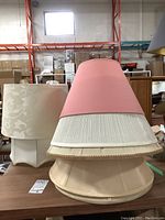 Photo showing six assorted fabric lampshades, including cream floral square shade, double-layered pink and white shade, and beige pleated shade.