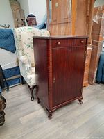 Full view of the mahogany cabinet showing single drawer above single door and the brass knobs and handle.