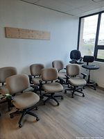 Six beige office chairs and two black stools in a room near window.