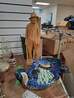 Photo showing wooden figure with hat standing and ceramic bird laying on table.