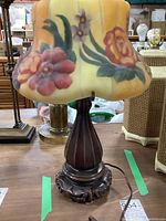 Frontal view of lamp showing the yellow-orange puffy glass shade with floral hand-painted design, wood base with ceramic ornamental bottom.